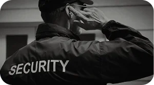 Security guard adjusting earpiece while wearing a uniform with “SECURITY” printed on the back, showing alertness.