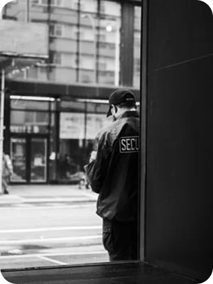 A security guard standing near a doorway, watching an urban street.